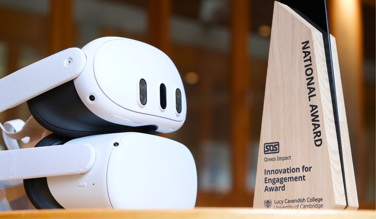 The image shows two white virtual reality headsets one on top of the other resting on a surface. Adjacent to the right, there's a wooden triangular award plaque with text that reads "NATIONAL AWARD", below which is a logo and additional text that appears to say "Innovation for Engagement Award" followed by "Lucy Cavendish College University of Cambridge". 