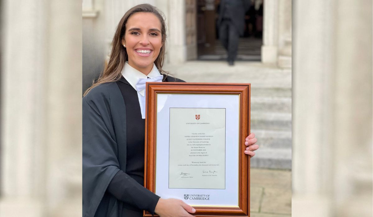Sophia holding a framed diploma from the University of Cambridge. She is standing outside the Senate House.