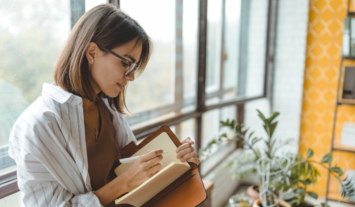 Young woman with short dark hair and glasses writing on notebook