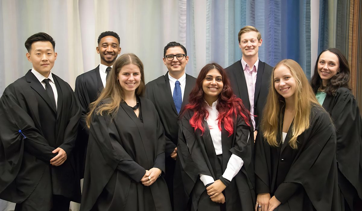 The image features a group of individuals dressed in academic robes, posing for their matriculation picture. Three are in the front row and four in the back row.